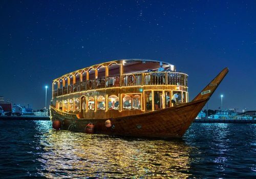 dhow-dinner-cruise-dubai-skyline.jpg Traditional dhow dinner cruise sailing under Dubai skyline at night with luxury lighting